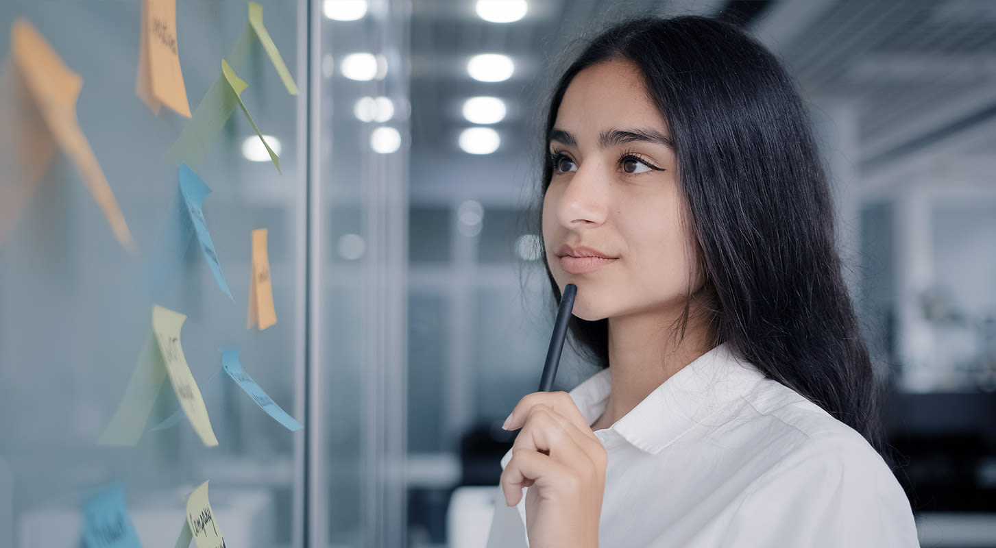 A woman wearing a white shirt studies a whiteboard filled with various sticky notes.